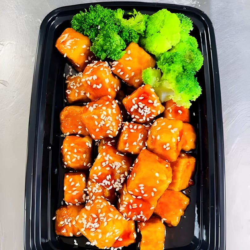Lotus's orange chicken with sesame seeds and a side of steamed broccoli in a black takeout container.