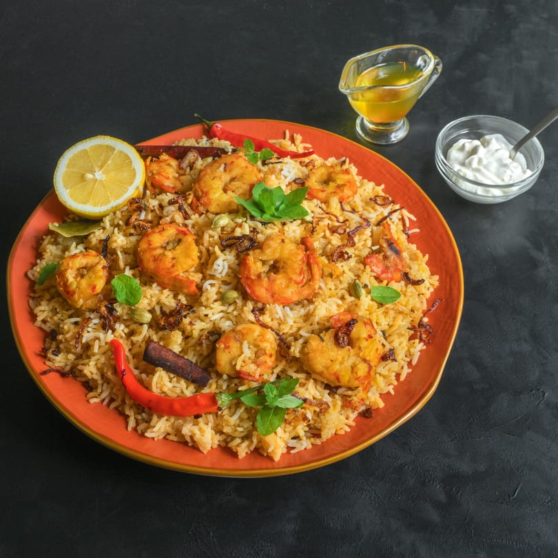 Shrimp biryani with rice, spices, lemon, mint, and chili on an orange plate, with sauces.