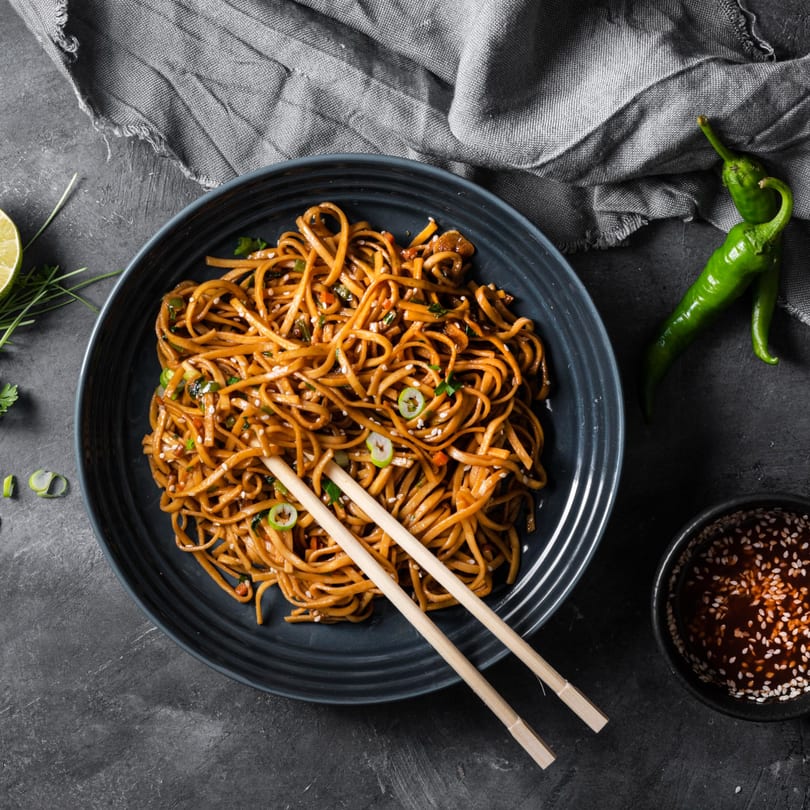 Lotus's Chinese noodles with green onions and sesame seeds, served with chopsticks and dipping sauce.