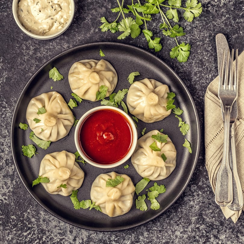 Overhead view of six Chinese dumplings with red sauce, cilantro, and a creamy dip.